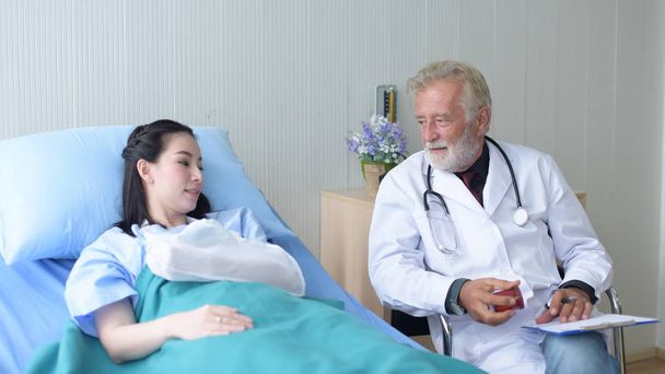 Ο γιατρός να φροντίζει και να ενθαρρύνει τον ασθενή στο γιατρό hospital.cheerful μιλούν με νεαρή γυναίκα ασθενή για την παρακολούθηση και έλεγχος μέχρι μετά από χειρουργική επέμβαση. - Φωτογραφία, εικόνα