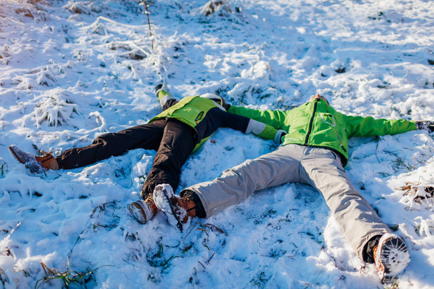 Giovane coppia innamorata sdraiata sulla neve e facendo angeli di neve. Persone felici che si divertono nella foresta invernale. Attività stagionali
 - Foto, immagini