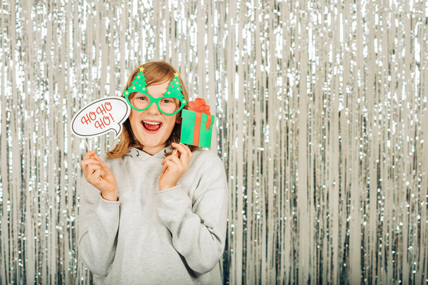 Vánoční portrét roztomilá holčička proti stříbrným pozadím, na sobě šedý svetr, drží slavnostní stran rekvizity pro photo booth - Fotografie, Obrázek