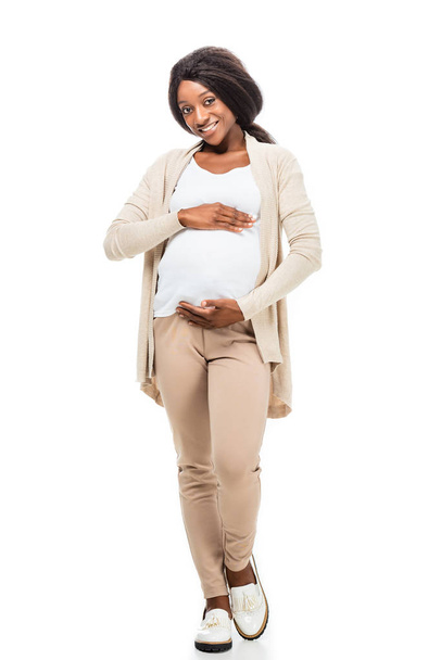 full length of smiling pregnant african american woman touching belly isolated on white - Foto, Imagen