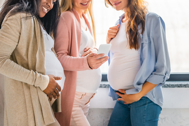 wielokulturowym, uśmiechając się kobiety w ciąży przy użyciu smartfona - Zdjęcie, obraz