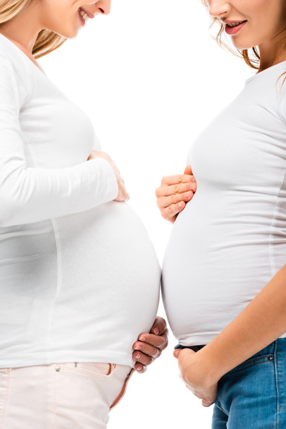abgeschnittene Ansicht von lächelnden Schwangeren, die eng beieinander stehen, isoliert auf weißem Grund  - Foto, Bild