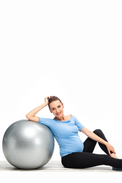 brown haired pregnant woman sitting on floor with fitness ball and looking to camera isolated on white - Photo, Image