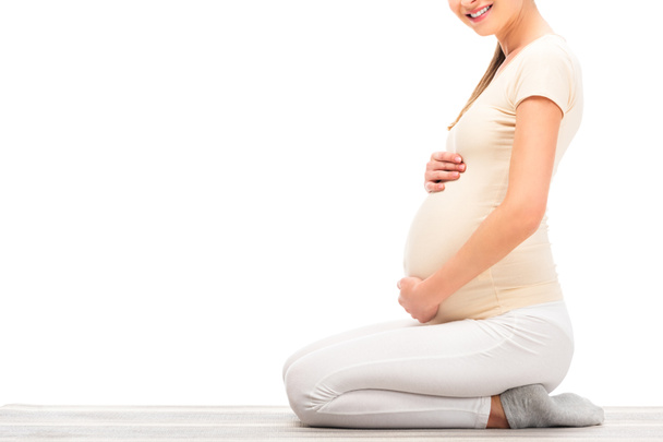 abgeschnittene Ansicht einer schwangeren Frau, die sitzt und die Hände auf dem Bauch hält, isoliert auf weiß - Foto, Bild