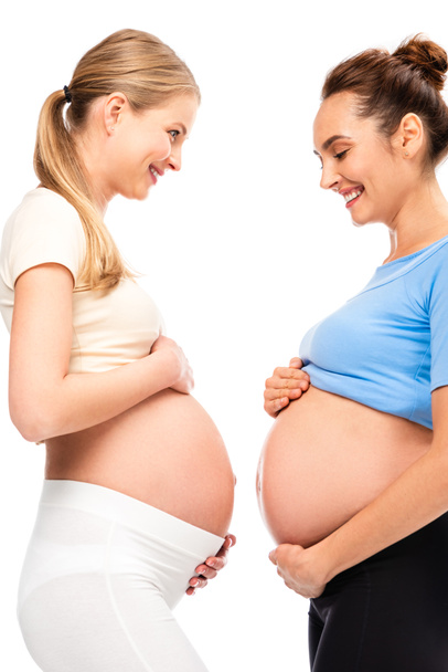 two pregnant women holding hands on bellies and smiling each other isolated on white - Foto, Bild