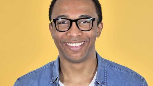 Zbliżenie na uśmiechający się Afryki człowiek w okularach na białym tle na żółtym tle - Materiał filmowy, wideo