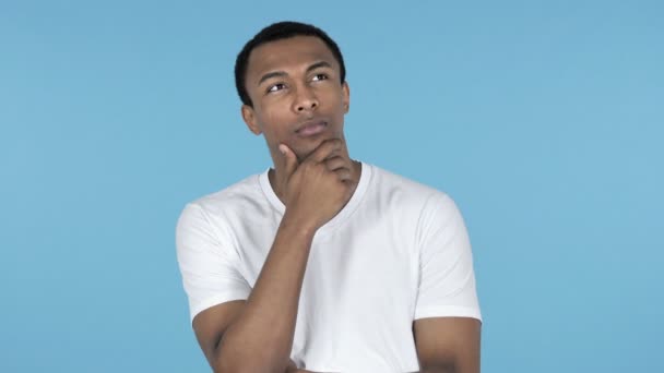 nachdenklicher junger afrikanischer Mann denkt isoliert auf blauem Hintergrund - Filmmaterial, Video