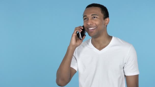 Mladý africký muž mluví na smartphone izolované na modrém pozadí - Záběry, video