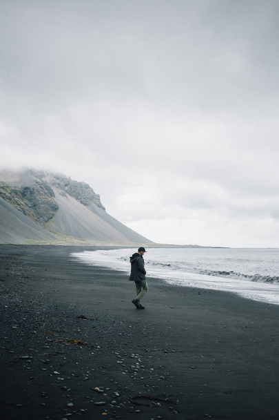 Lonely man walks on grey black volcanic sand beach - 写真・画像