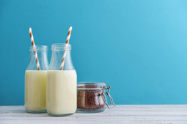 Two bottles vegetarian quinoa milk with quinoa in jar on blue background - Foto, afbeelding