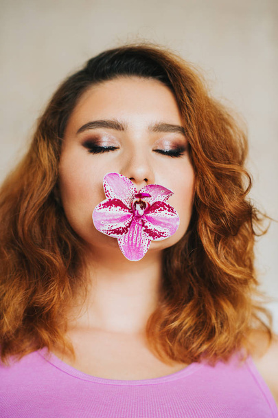 Nahaufnahme Porträt einer jungen Frau mit rosa Orchideenblume im Mund - Foto, Bild