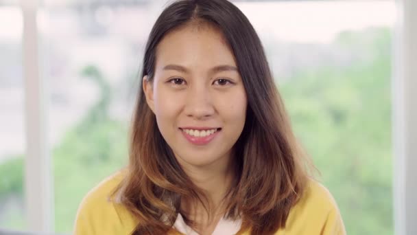 Teenager asiatische Frau glücklich lächelnd und blickend in die Kamera, während sie in ihrem Wohnzimmer zu Hause entspannen. schöne asiatische junge Frau mit entspannter Zeit zu Hause Konzept. - Filmmaterial, Video