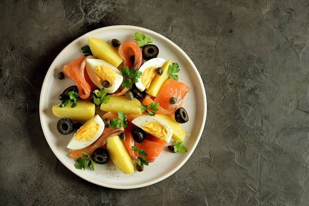 Ensalada de salmón salado, patatas hervidas, huevos de pollo con aceitunas, alcaparras, perejil y aceite de oliva
. - Foto, Imagen