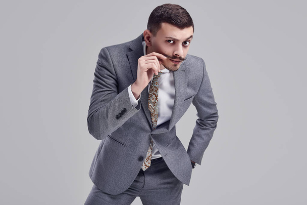 Porträt eines hübschen jungen selbstbewussten arabischen Geschäftsmannes mit schickem Schnurrbart im modischen grauen Ganzanzug auf Studiohintergrund - Foto, Bild