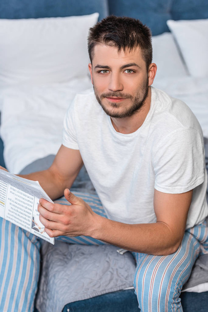 high angle view of handsome man holding newspaper in bed in morning at home - Фото, изображение