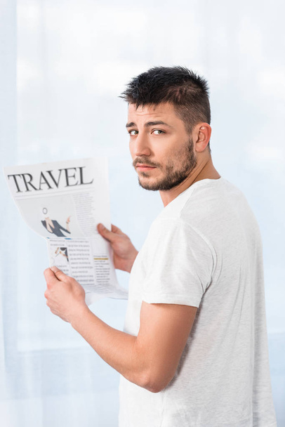 hombre guapo sosteniendo periódico de viaje en la mañana en casa y mirando a la cámara
 - Foto, Imagen