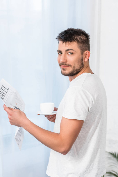 handsome man reading travel newspaper and holding cup of coffee in morning at home - Foto, immagini