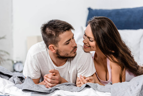 girlfriend and boyfriend in pajamas lying on bed and going to kiss in bedroom - Foto, afbeelding