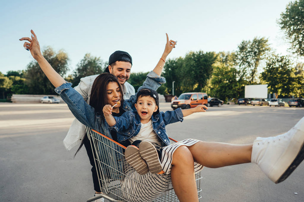 Young dad carries mom and son in a cart on the parking lot - Photo, Image