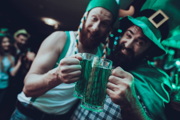 Saint Patrick's Day Party. Group of Friends is Celebrating. People is Drinking a Green Beer. Friends is Young Men and Woman. Drunk Men Toast with Each Other. People Wearing a Green Hats. Pub Interior. - Foto, afbeelding