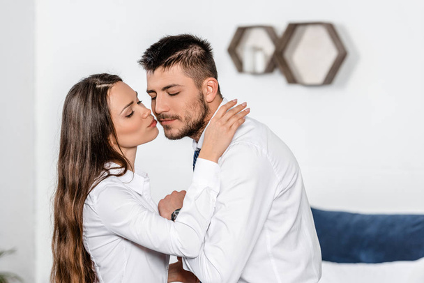 side view of girlfriend kissing boyfriend in morning in bedroom before work - Photo, Image