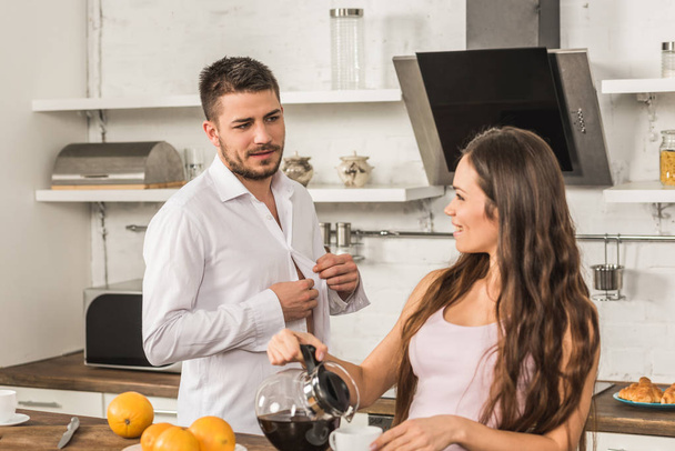 petit ami boutonnage chemise et petite amie verser du café dans la tasse à la maison, concept d'inégalité
 - Photo, image