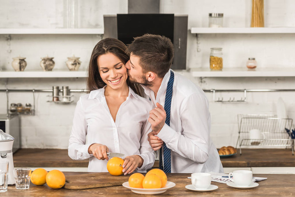 朝のキッチン、ジェンダー ステレオタイプ概念で彼女切削オレンジ中のガール フレンドのキスの彼氏 - 写真・画像