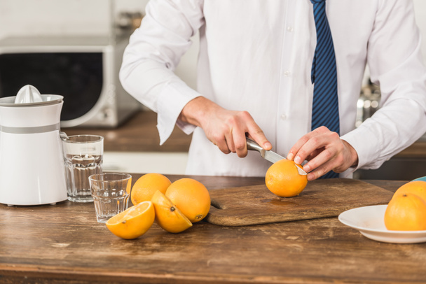 cropped image of man cutting oranges for juice in morning at kitchen - Foto, Bild