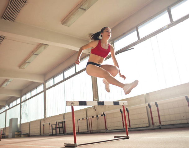 Athlete woman jumping over the racetrack - Foto, Imagen