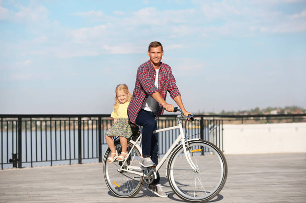 Father and daughter riding bicycle outdoors on sunny day - Zdjęcie, obraz