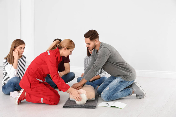 Group of people with instructor practicing CPR on mannequin at first aid class indoors - Фото, изображение