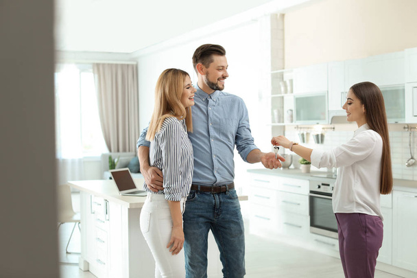 Female real estate agent giving house key to couple indoors - Φωτογραφία, εικόνα