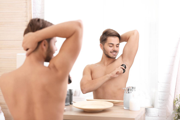 Handsome young man applying deodorant in bathroom - Photo, image