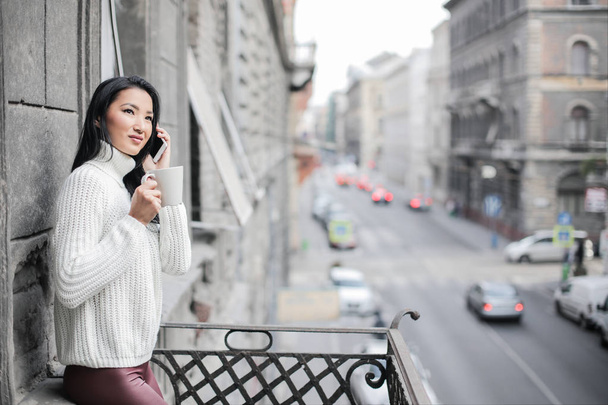 attraente asiatico donna avendo un caffè e tenendo il suo telefono in il balcone
 - Foto, immagini