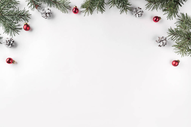 Kreativer Rahmen aus Tannenzweigen auf weißem Hintergrund mit roter Dekoration, Tannenzapfen. Weihnachts- und Neujahrsthema. flache Lage, Draufsicht - Foto, Bild