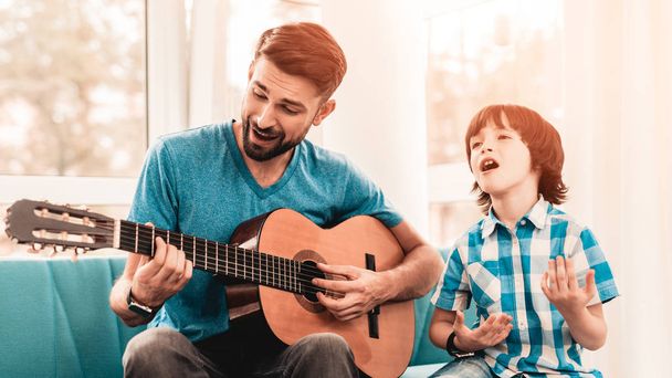 Young Bearded Father Playing on Guitar with Son. Happy Family Concept. Musician at Home. Young Boy in Shirt. Modern Hobby Concept. Music and Songs Concepts. Smiling Man. - Foto, immagini