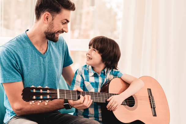 Young Bearded Father Playing on Guitar with Son. Happy Family Concept. Musician at Home. Young Boy in Shirt. Modern Hobby Concept. Music and Songs Concepts. Smiling Man. - Фото, изображение