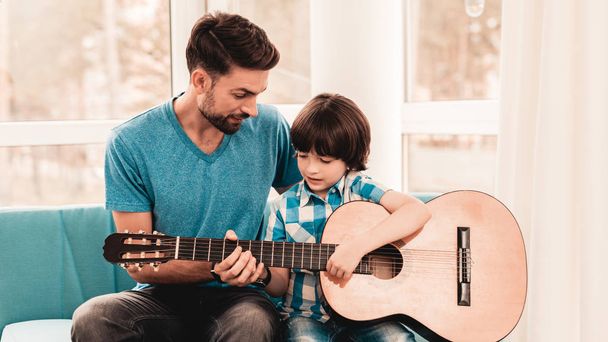 Young Bearded Father Playing on Guitar with Son. Happy Family Concept. Musician at Home. Young Boy in Shirt. Modern Hobby Concept. Music and Songs Concepts. Smiling Man. - Foto, immagini