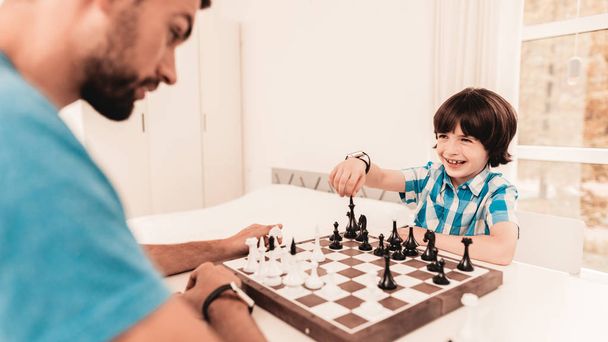 Bearded Father and Son Playing Chess on Table. Happy Family Concept. Board on Table. Young Boy in Shirt. Indoor Joy. Board Games Concept. Modern Hobby Concept. Black and White Figures. - Zdjęcie, obraz