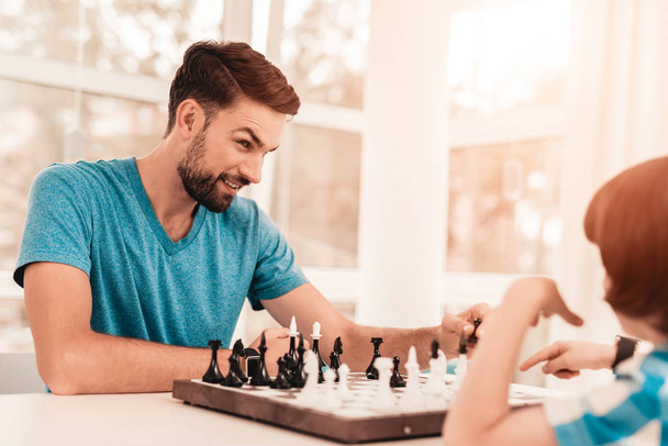 Bearded Father and Son Playing Chess on Table. Happy Family Concept. Board on Table. Young Boy in Shirt. Indoor Joy. Board Games Concept. Modern Hobby Concept. Black and White Figures. - 写真・画像