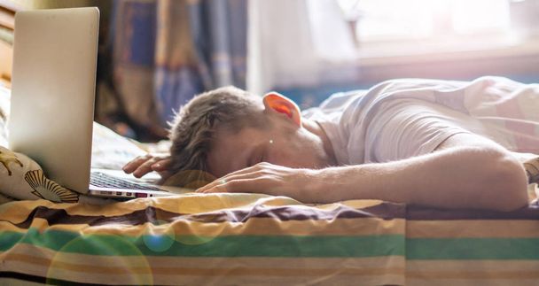 młody człowiek leży i śpi na łóżku w słoneczny poranek po pracy na laptopie w nocy f - Zdjęcie, obraz