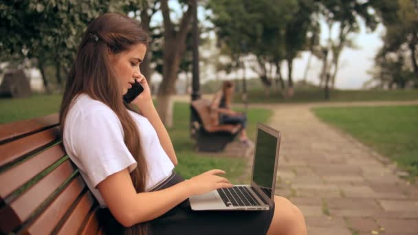 woman typing on laptop talking by phone - Felvétel, videó