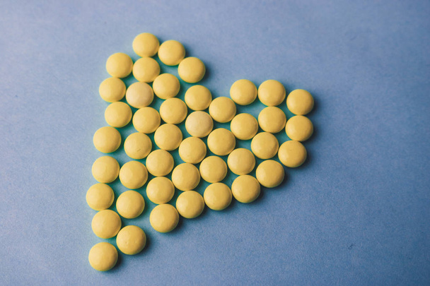 Small medical pharmaceptic round yellow pills, vitamins, drugs, antibiotics in the form of a heart on a blue background, texture. Concept: medicine, health care, heart disease. Flat lay, top view - Foto, imagen