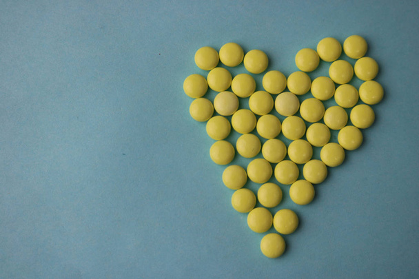 Küçük tıbbi pharmaceptic yuvarlak sarı haplar, vitaminler, ilaçlar, antibiyotik mavi bir arka plan doku üzerinde bir kalp şeklinde. Konsept: tıp, sağlık, kalp hastalığı. Düz yatıyordu, en iyi görünümü - Fotoğraf, Görsel