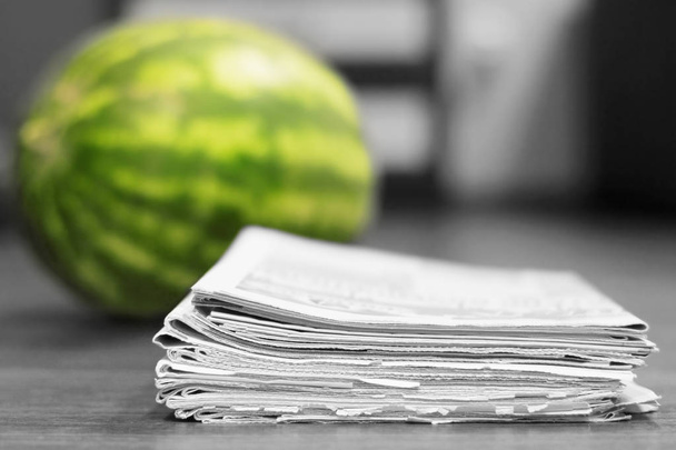 Newspapers and watermelon. Daily papers stacked in pile and fresh juicy fruit as concept for latest news and sensation. Tabloid journals pages with headlines and articles, selective focus on paper - Photo, Image