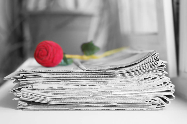 Sanomalehtiä ja ruusuja. Monet paperit uutisia pinottu kasaan ja punainen kukka, sivunäkymä
 - Valokuva, kuva