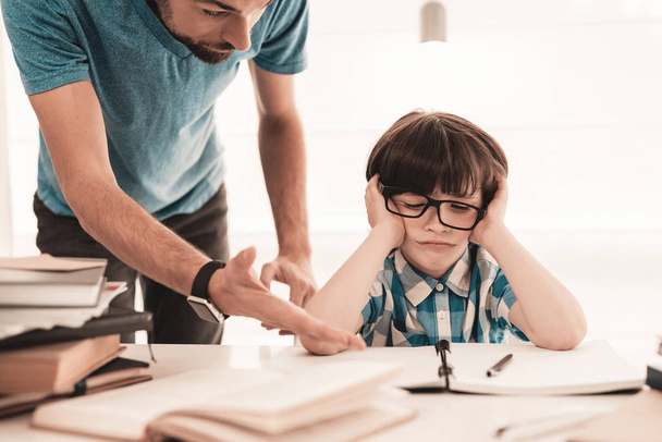 Little Boy in Glasses Doing Homework with Father. Education at Home. White Table in Room. Sitting Boy. Young Father. Lesson at Home. Education Concept. Writing in Notebook. Boy in Shirt. - Foto, afbeelding