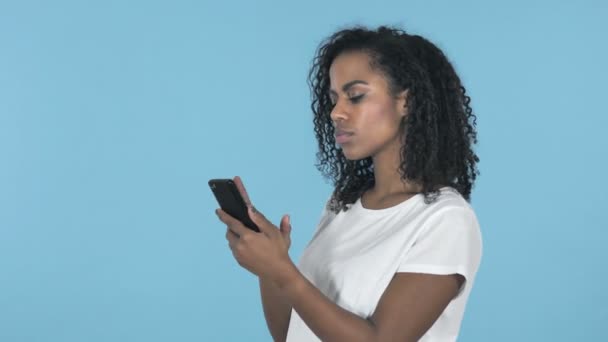 African Girl Excited for Success while Using Smartphone Isolated on Blue Background - Πλάνα, βίντεο