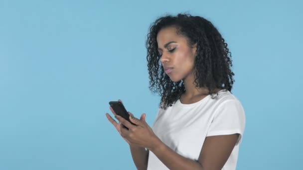 African Girl in Shock while Using Smartphone Isolated on Blue Background - Πλάνα, βίντεο