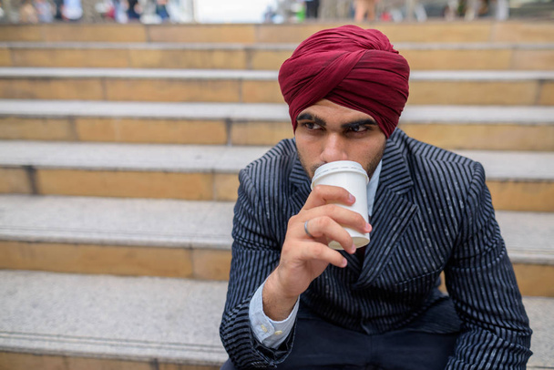Hintli işadamı açık havada kahve yudumlarken şehirde oturan - Fotoğraf, Görsel